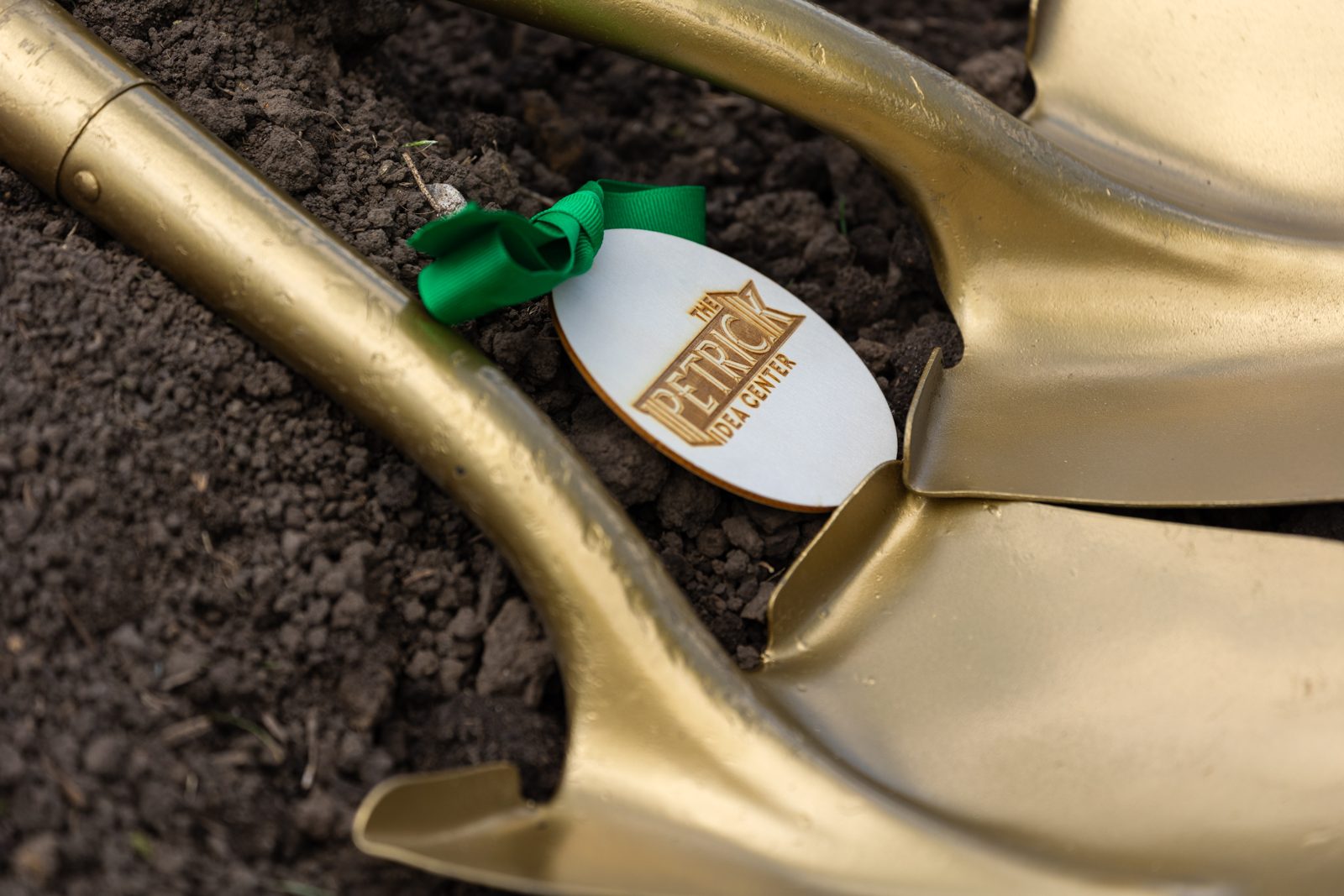 A gold shovel with a Petrick Idea Center tag resting in fresh soil