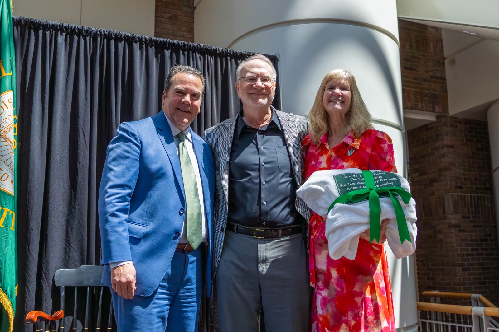 Ann and Alan Fisher on stage with a university leader, holding a gift wrapped in green ribbon