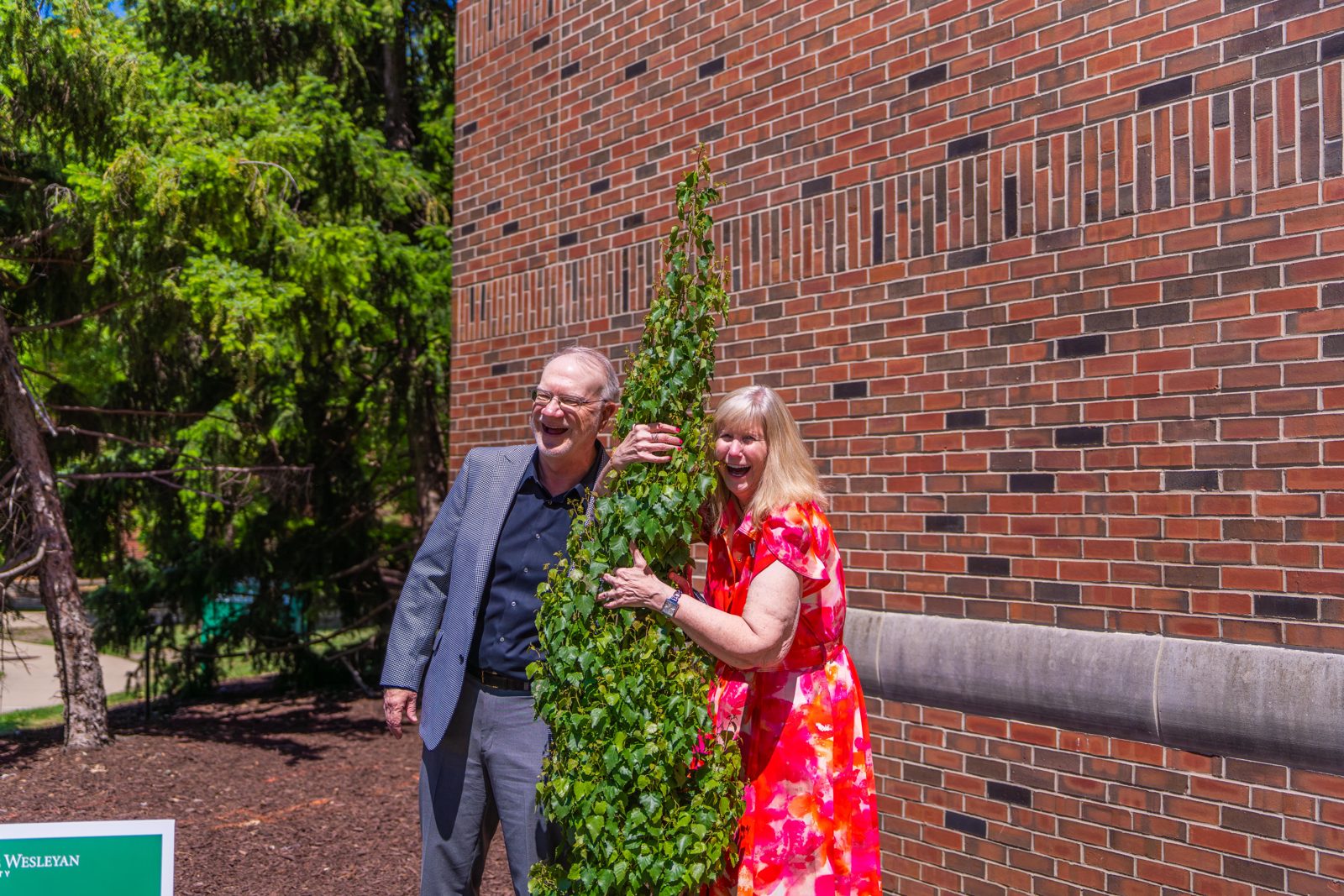 Ann and Alan Fisher laughing beside an ivy topiary outside a campus building